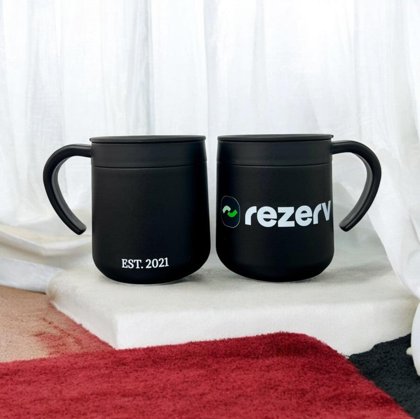 Multiple custom coffee mugs in various colors with corporate logos on modern office setting